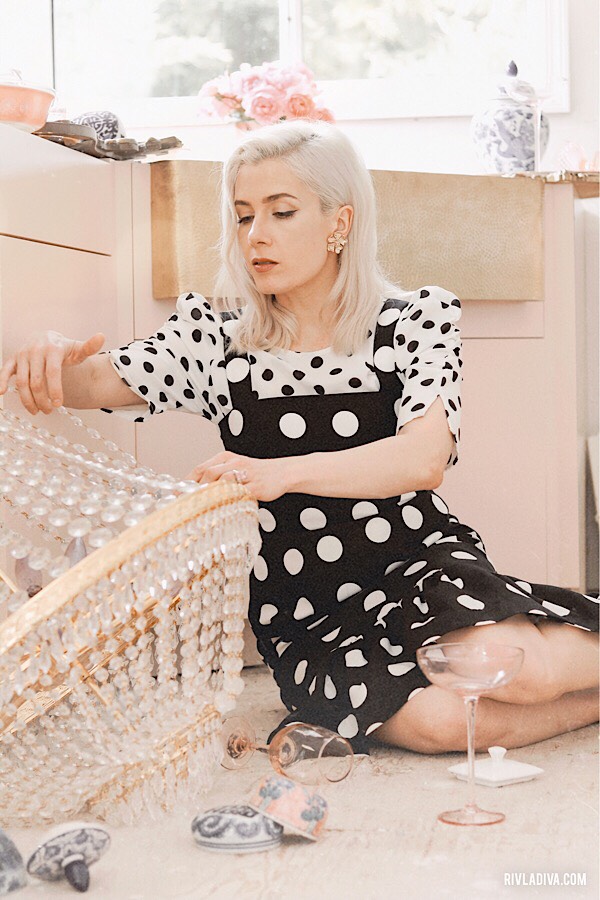 Woman wearing a Polka dot dress with a polka dot shirt. Black dress and white shirt outfit. Sitting in a blush kitchen.