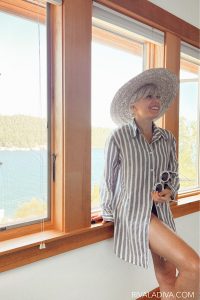 Woman wears hat and smiling in a blue and white striped button-up blouse from summer.